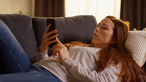Close-Up-Of-Woman-Lying-On-Sofa-At-Home-At-Streaming-Or-Watching-Movie-Or-Show-Or-Scrolling-Internet-On-Mobile-Phone-7